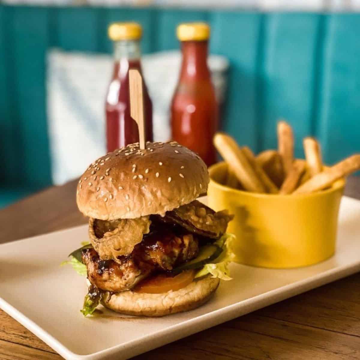 Dijon Cafe BBQ Chicken Burger with fries on the side and 2 bottles of red sauce