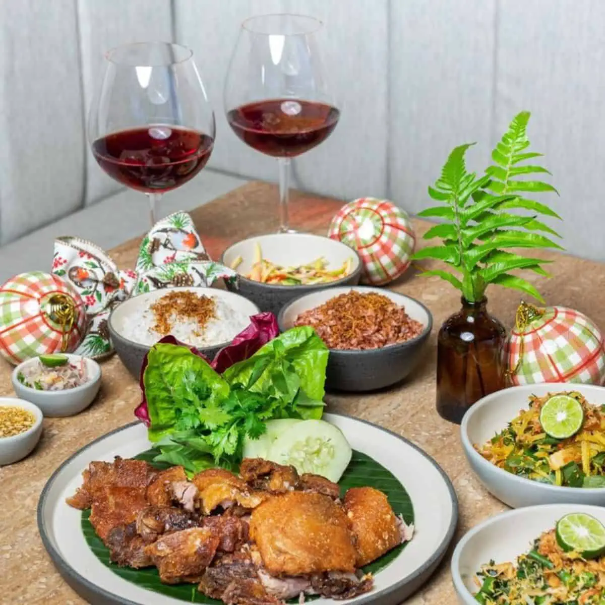 A table filled with Indonesian dishes and two half filled glasses of red wine with christmas balls as a decor in Ulekan Bali