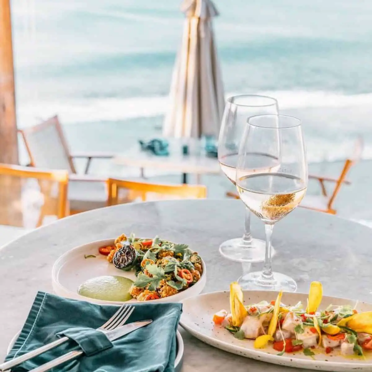 Delicious plates for lunch with two glasses of champagne, fork and knife on the side and a beach view at Ulu Cliffhouse