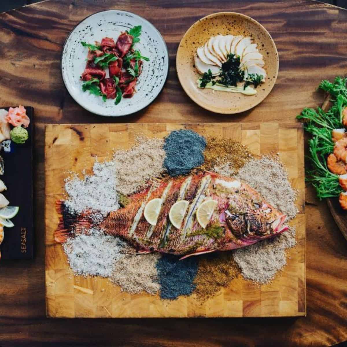 Grilled fish, prawns, and other seafood on a woody table of Seasalt Seminyak in different servings and garnishes