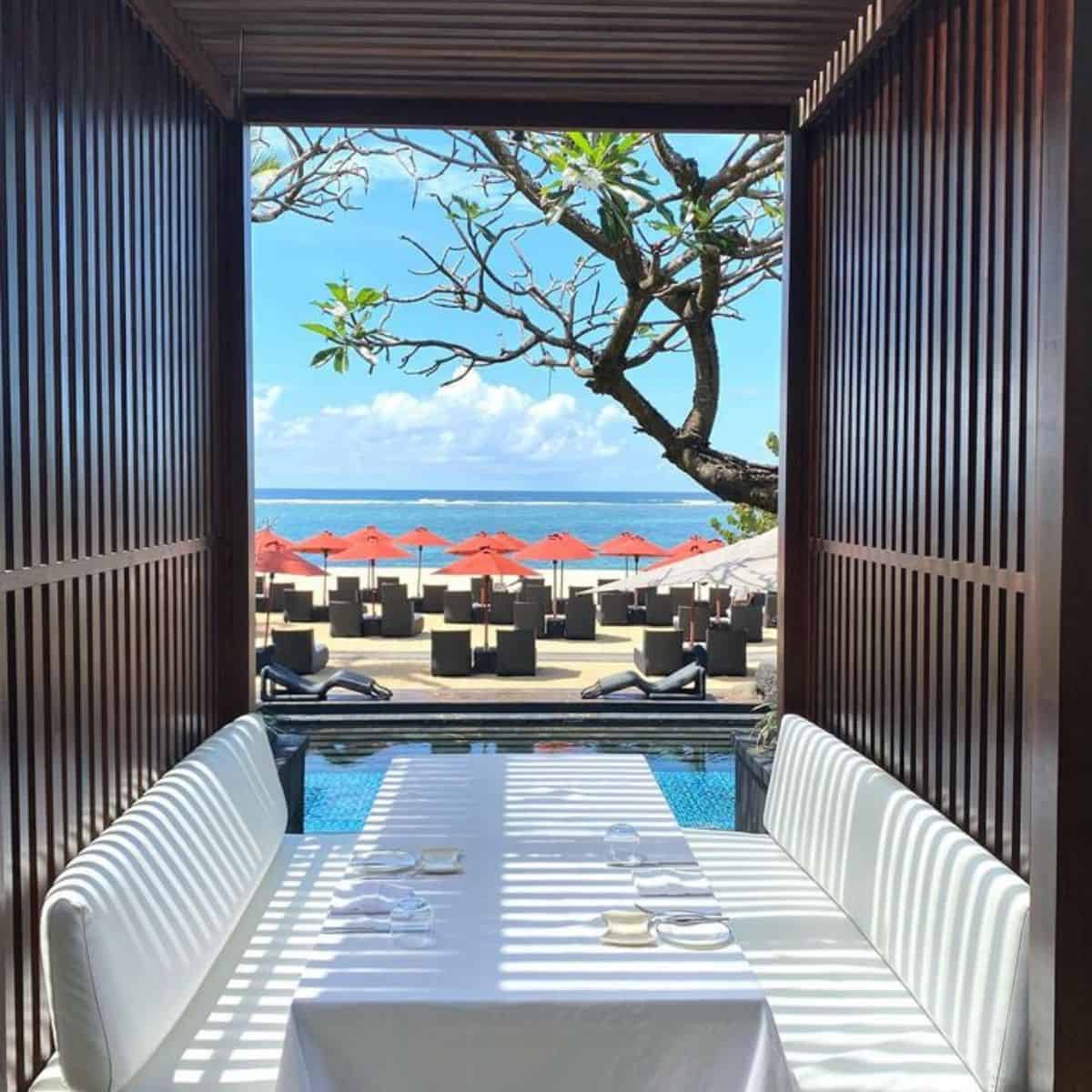 Kayaputi Restaurant’s outdoor dining table in white linen and red beach umbrellas in the front view
