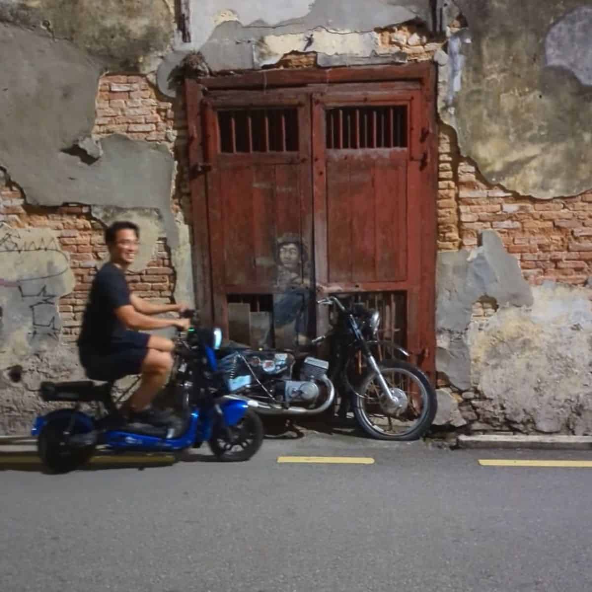 Ruiz zooming in on an ebike beside Boy on Motorbike street art Georgetown