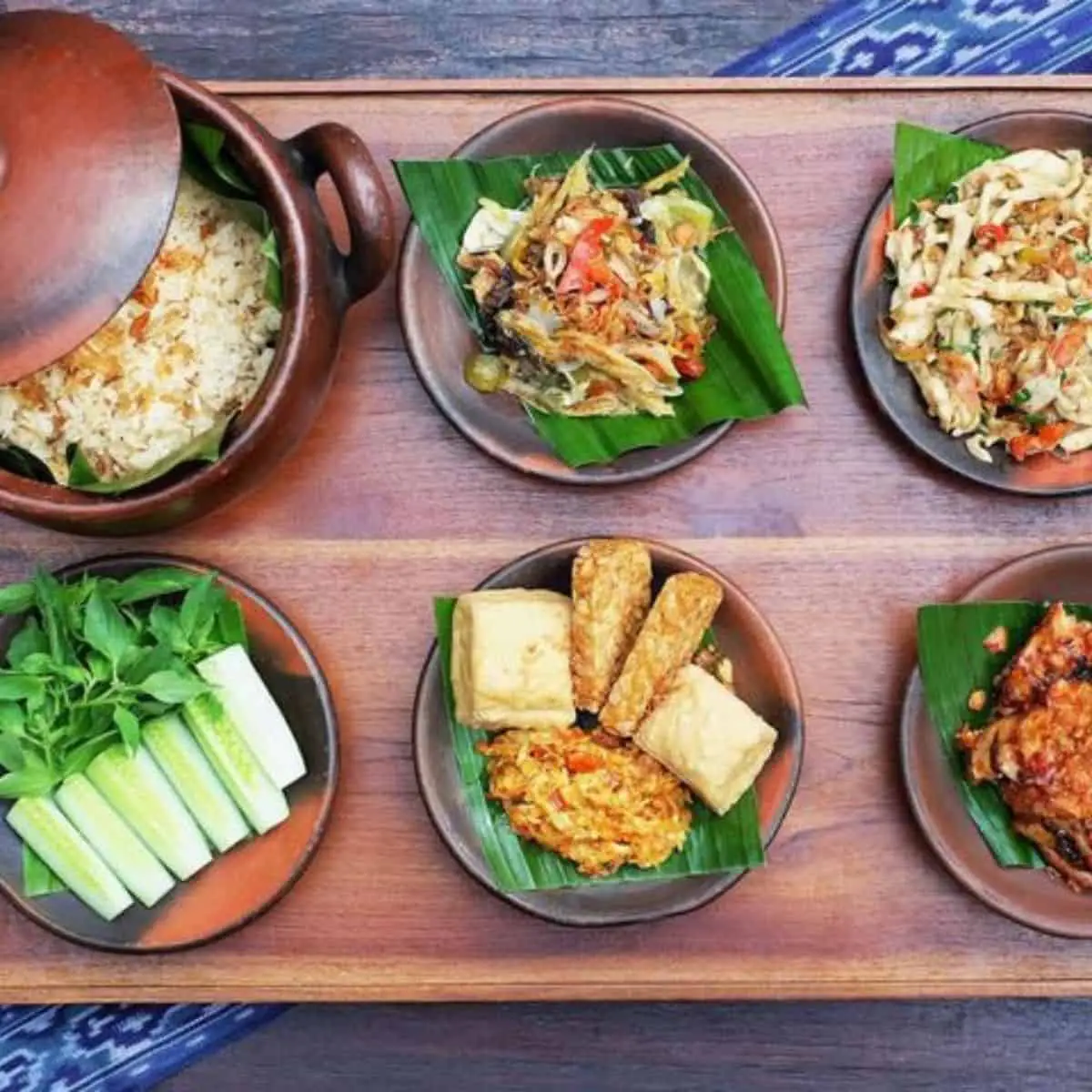Six servings of delectable Indonesian cuisines with banana leaf underneath in wooden plates and pot in Kaum