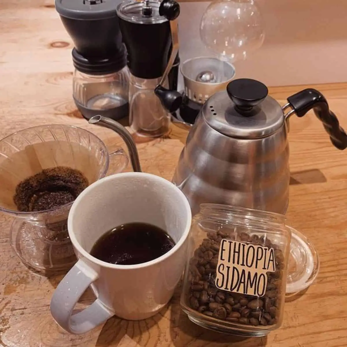 Coffee beans in a transparent jar with a cup of coffee and other coffee maker equipments laid in the table of PBC Coffee