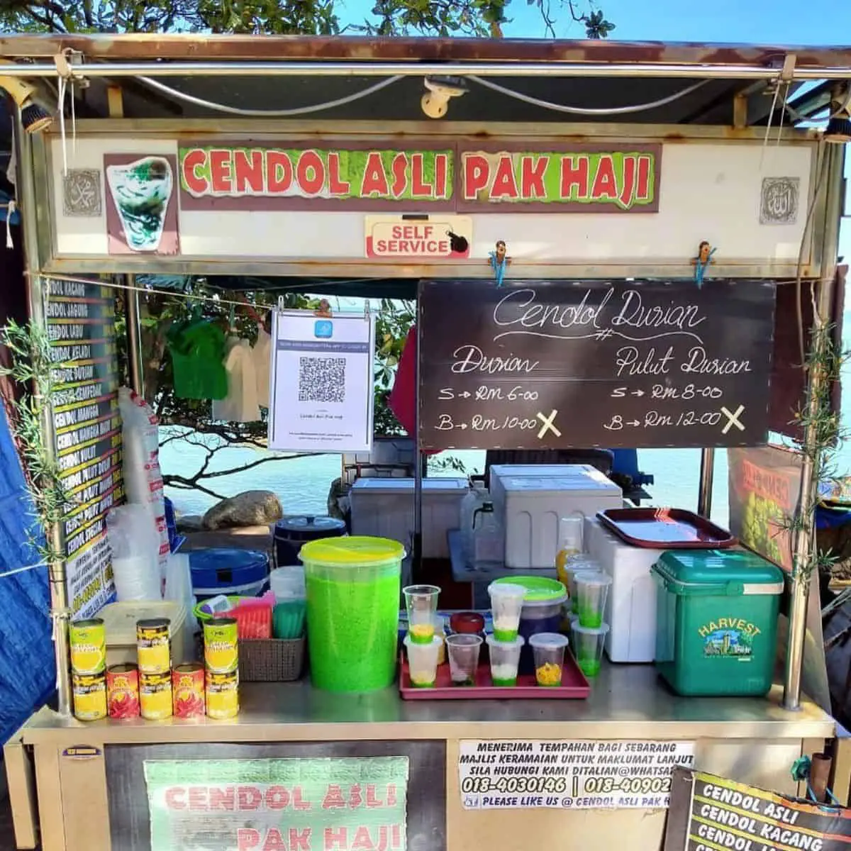 Asli Pak Haji stall with plastic glasses and canned milk on display in green and yellow hues