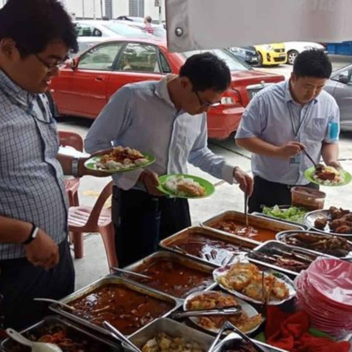 Employees lining up at Kak Ema's stall for lunch with different Malaysian food trays to be selected