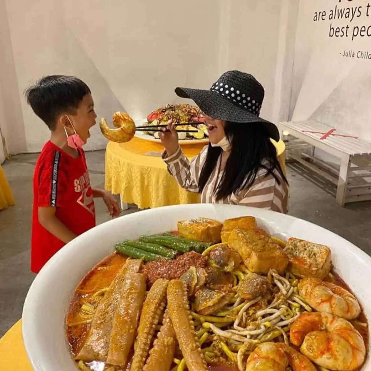 Mom playfully feeding her son a large piece of clean shrimp from a large bowl of seafood in Wonderfood Museum