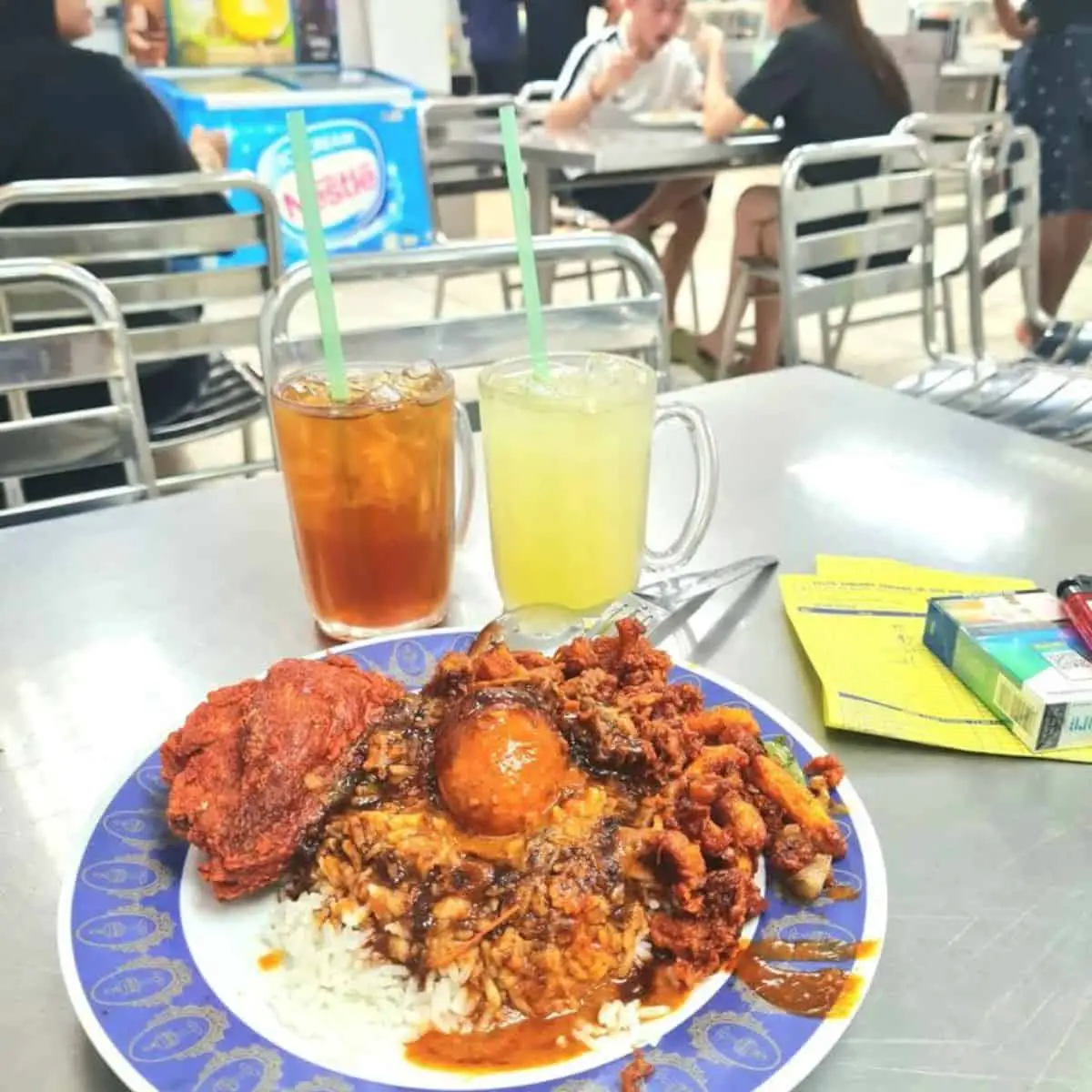 One Nasi Kandar plate of Pelita with two cold coloured drinks in an open crowded area