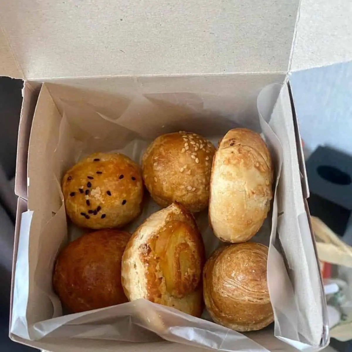 Six delectable baked pastries from Seng Seng Hiang with black and white sesame seeds on top in a grey box
