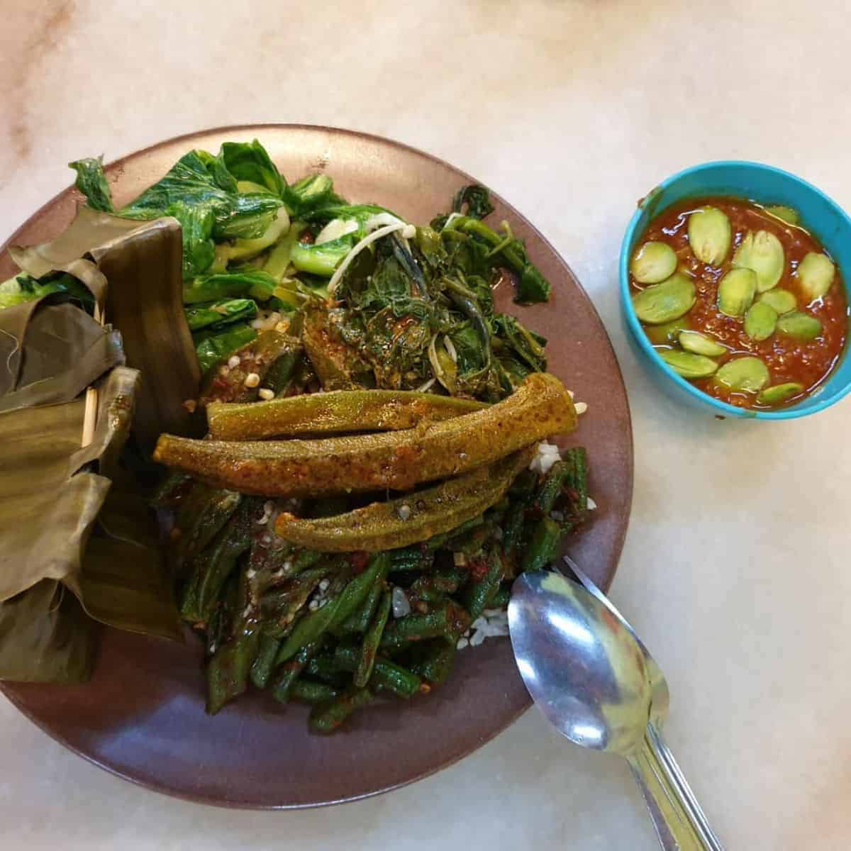 One serving of a vegetarian dish in a brown plate and a spicy sauce in a small blue bowl from Evergreen Penang