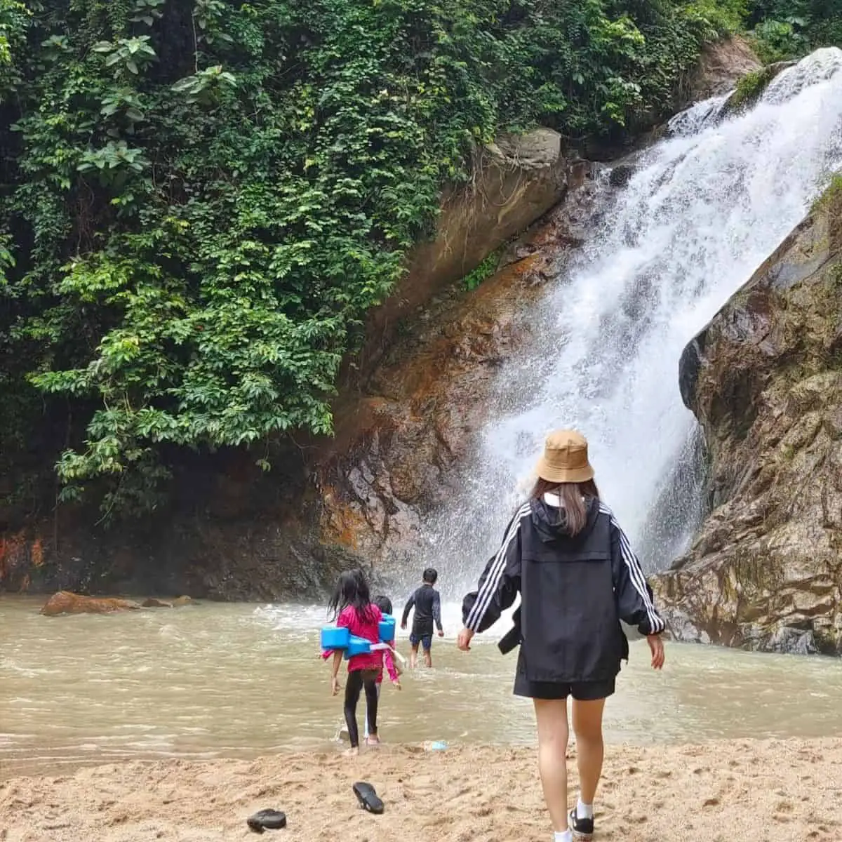 Sunga Dua Waterfall in Penang with raging waters from the mountains and a lady with a bucket hat in the middle