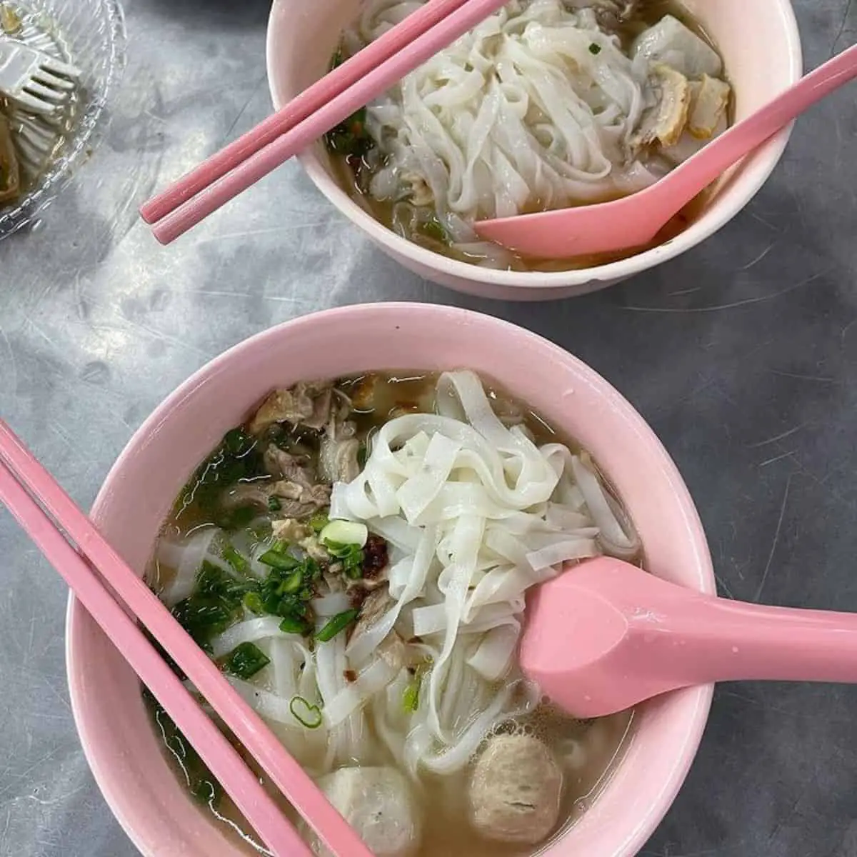 Two bowls of scrumptious Penang street food with pink spoons and chopsticks