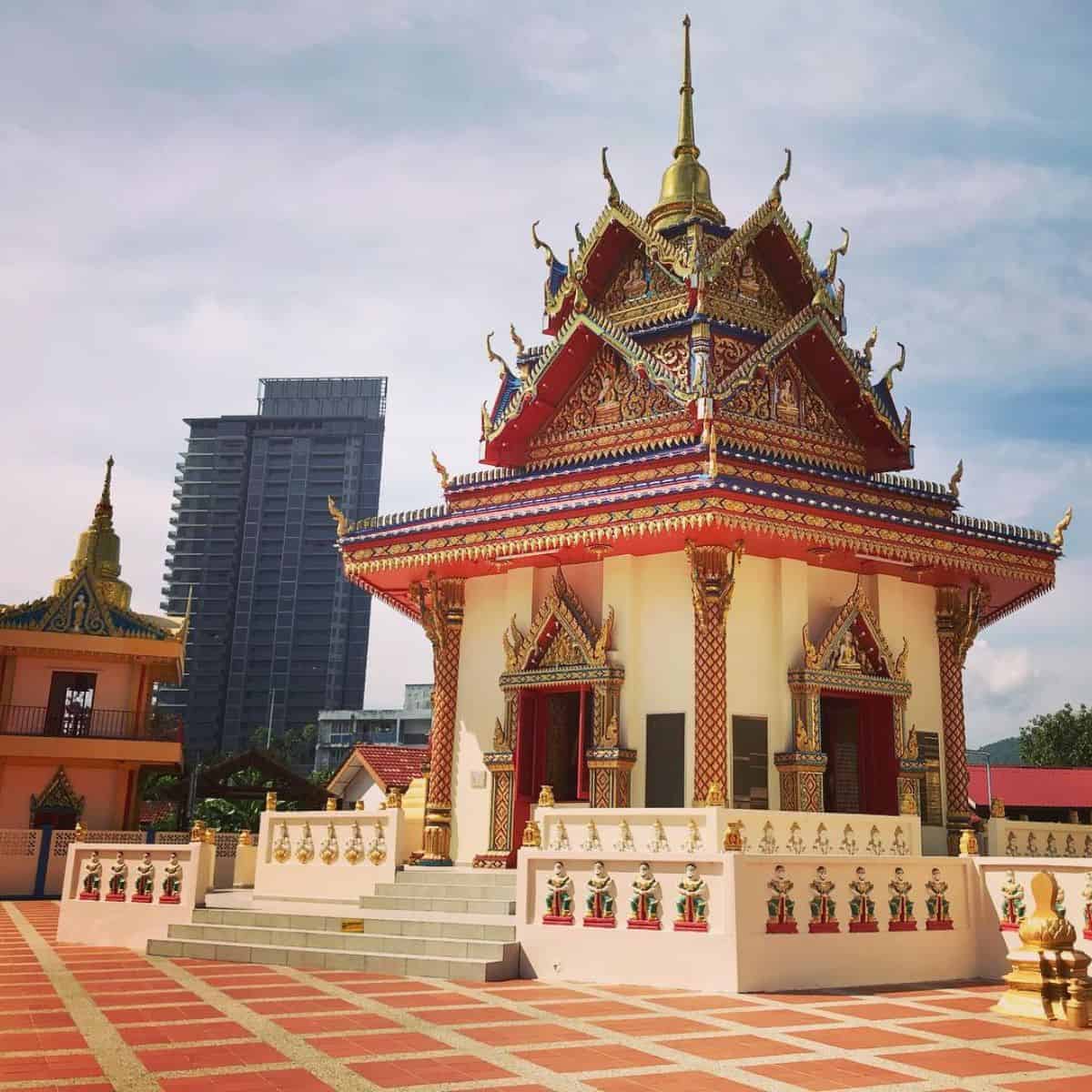 Penang Temple in red and gold colours with a towering building in the background